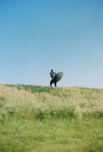 san francisco man standing on green grass mountain holding long surfboard ocean beach
